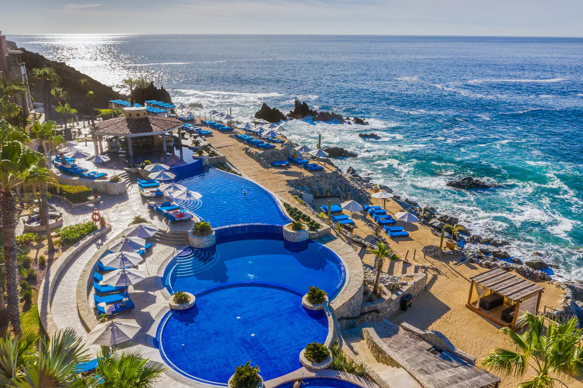 tres piscinas con camastros a los costados que dan a una vista a un acantilado frente al mar de cortes
